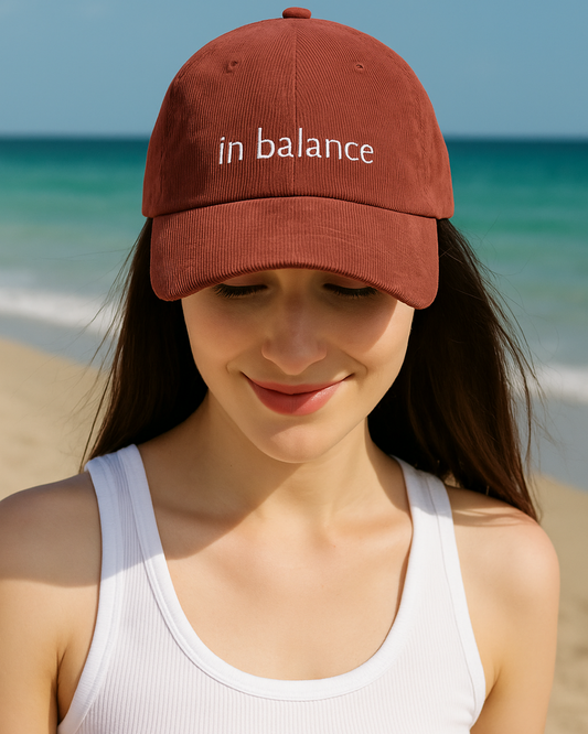 Woman wearing a brown cap with 'in balance' text on a beach